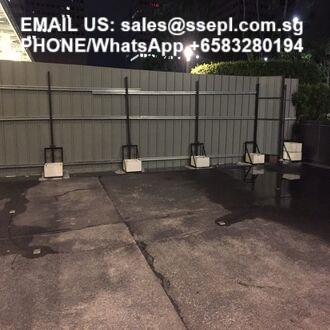 Nighttime parking lot with a row of metal barriers on white bases along a fence; wet asphalt surface.