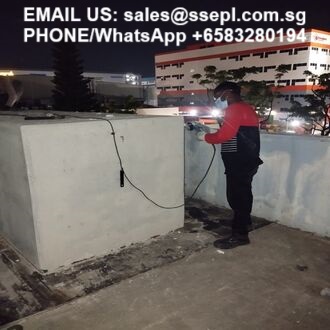 Nighttime rooftop with a man in a red jacket inspecting cables along a concrete parapet; contact email and phone number are overlaid at the top.