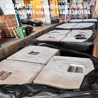 Row of square concrete blocks with built-in handles, stacked on pallets and wrapped in black plastic in a construction yard.