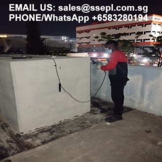 Nighttime scene of a worker in a red and black jacket fixing electrical cables on a rooftop, with contact email and phone number overlaid.