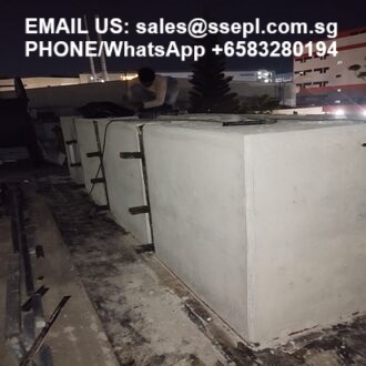 Night rooftop scene with several large rectangular white concrete water tanks; a worker visible in the background, with contact email and WhatsApp number displayed at the top surface edge.