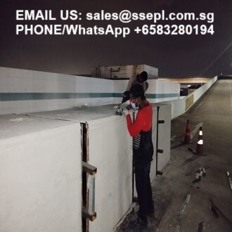Two workers on a concrete barrier at night, one in a red shirt using a tool; contact email and WhatsApp number appear in the upper left corner.