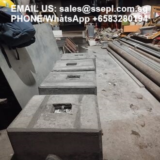 Construction site with large gray concrete blocks on the ground and metal pipes stacked to the right; white text at top shows an email and WhatsApp contact.