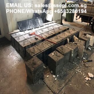 Construction site showing a concrete block foundation with a metal rebar frame on top and scattered debris.