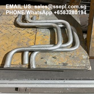 Bent metal tubes arranged on a worn yellow workbench with overlay contact text (EMAIL US: sales@... PHONE/WhatsApp +65...).