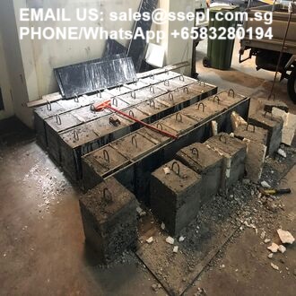 Industrial workshop with rows of rebar-reinforced concrete blocks and metal framing; concrete debris on the floor, plus a white text overlay with an email and WhatsApp contact.